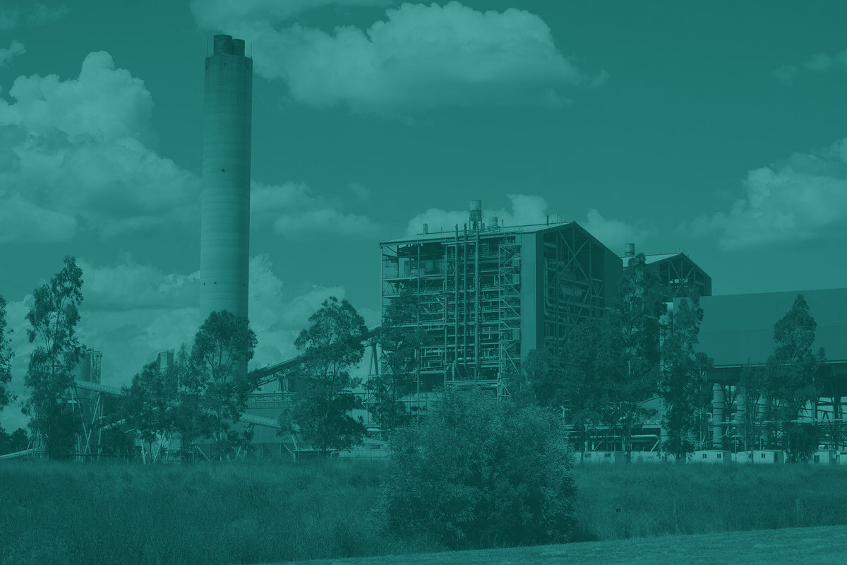 Industrial building with a tall smokestack and surrounding trees under a cloudy sky.